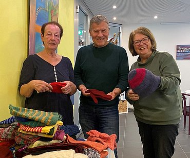 Frauen stehen mit Mitarbeiter von der Aufbaugilde und ihren gestrickten Sachen im Bild